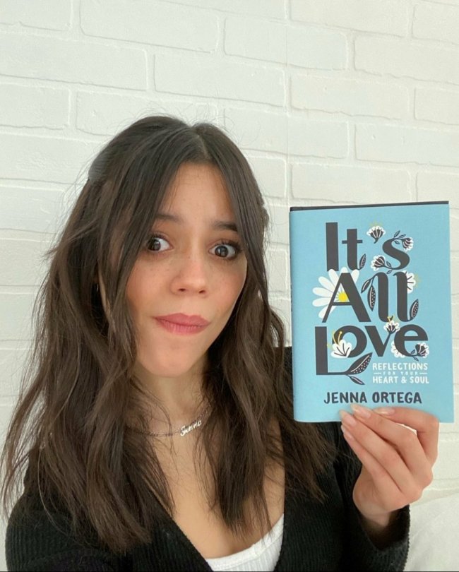 jenna-ortega-livro Jenna Ortega segurando o seu livro 'It's All Love' com capa azul