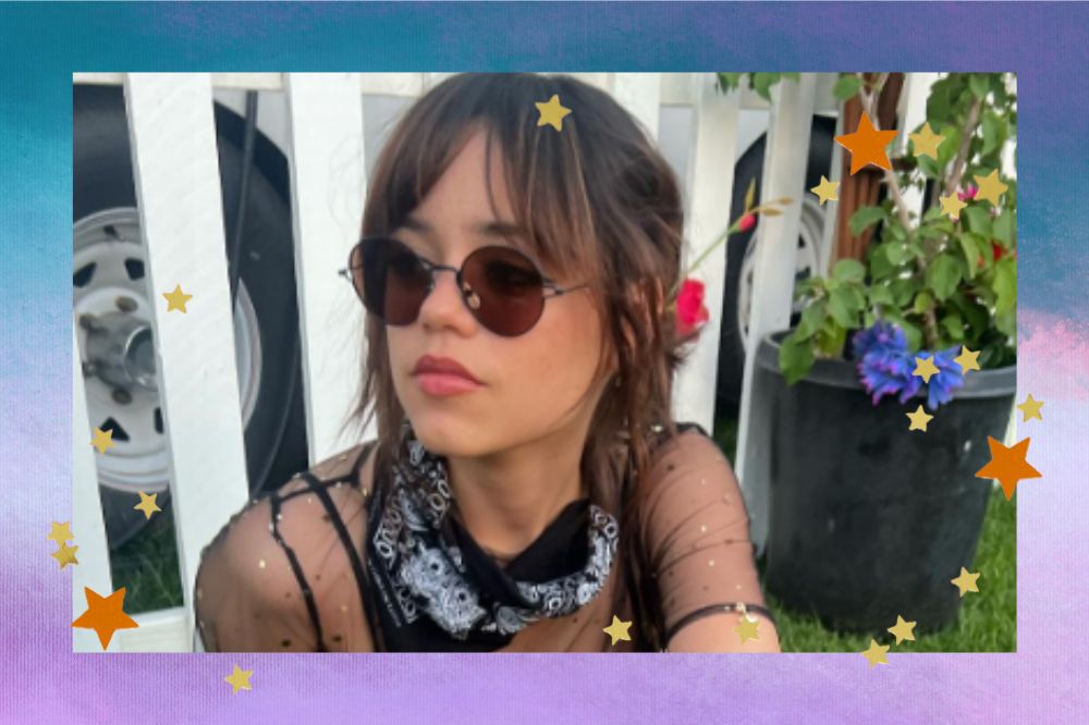 Montagem com fundo azul e lilás. No meio da imagem, Jenna Ortega está com um óculos de sol olhando para o lado esquerdo. Ela usa uma bandana preta no pescoço e uma blusa transparente. O cabelo está preso e a franja solta. Há flores no lado direito.