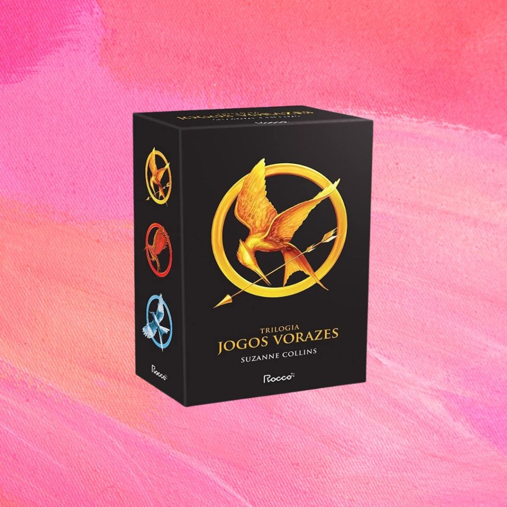 Jogos Vorazes Imagem do box de livros da saga Jogos Vorazes. Fundo rosa.