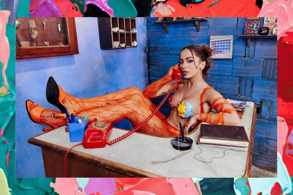 anitta sentada em uma cadeira, com as pernas na mesa em seu novo clipe