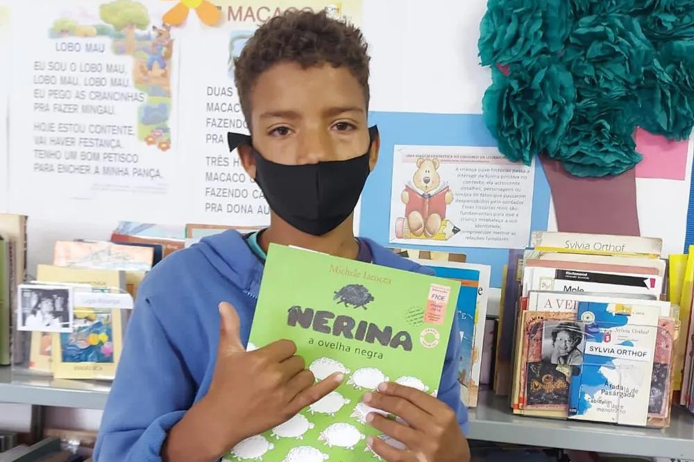 Menino usa máscara e segura livro na mão