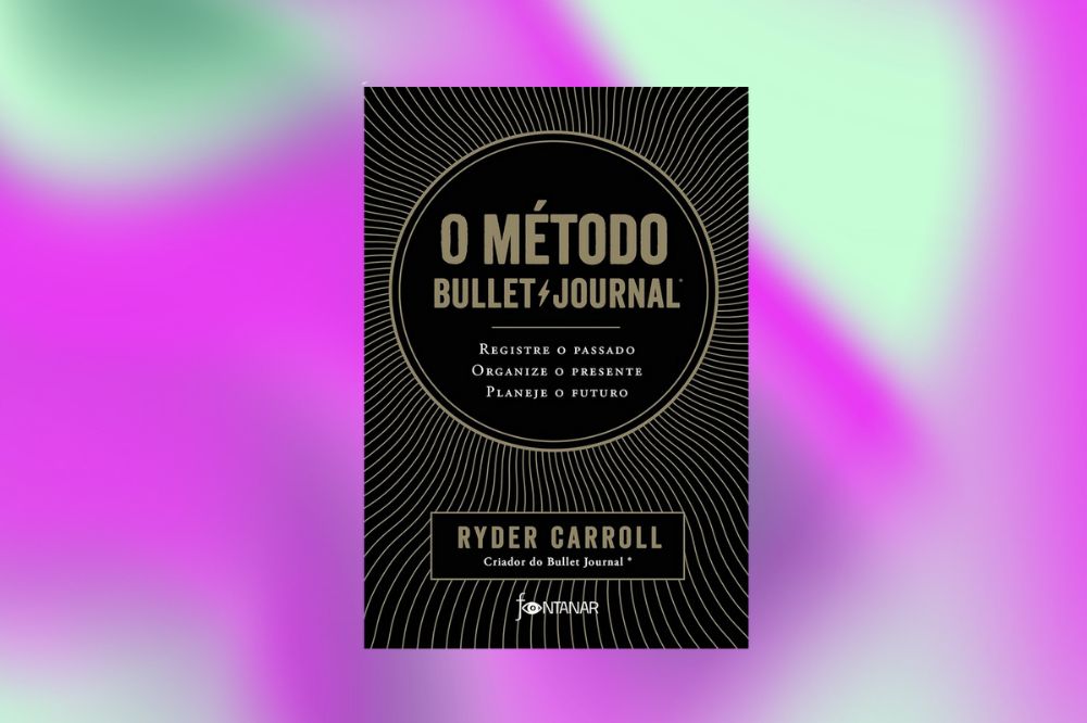 Em um fundo rosa, roxo e verde, tem no centro a capa preta com detalhes dourados do livro "O método Bullet Journal: Registre o passado, organize o presente, planeje o futuro"