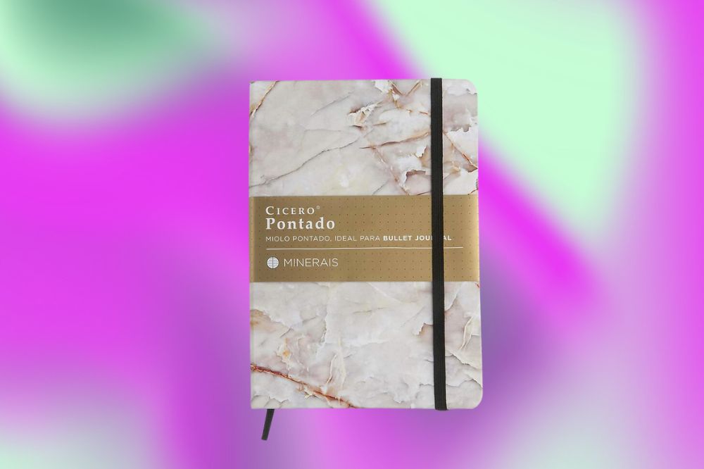 Em um fundo roxo, rosa e verde, no centro aparece um caderno com a estampa de um mármore nas cores brancas, marrom e cinza