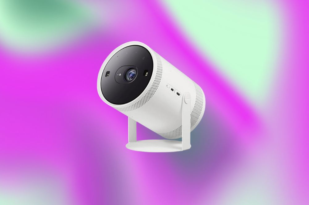 Em um fundo verde e roxo, o projetor é cilíndrico, branco, com a base da frente, onde fica a lente, preto
