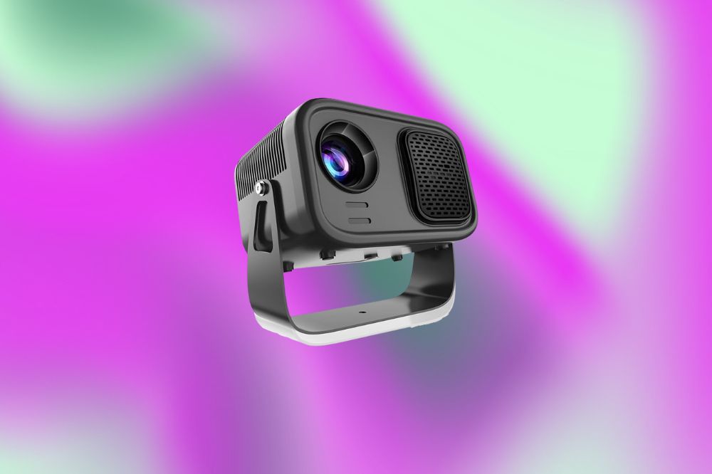 Em um fundo verde e roxo, há um mini projetor preto, com o visor do lado direito e uma alça em baixo para segurar