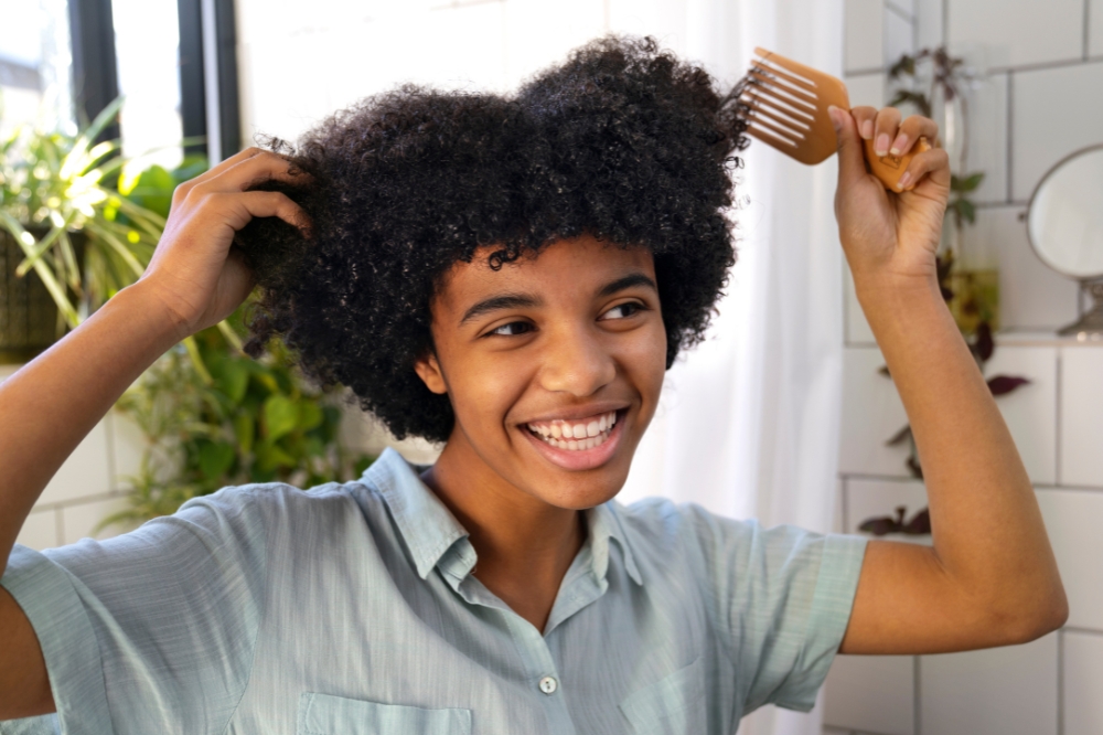 Pessoa com cabelo crespo penteando os fios em frente ao espelho e sorrindo