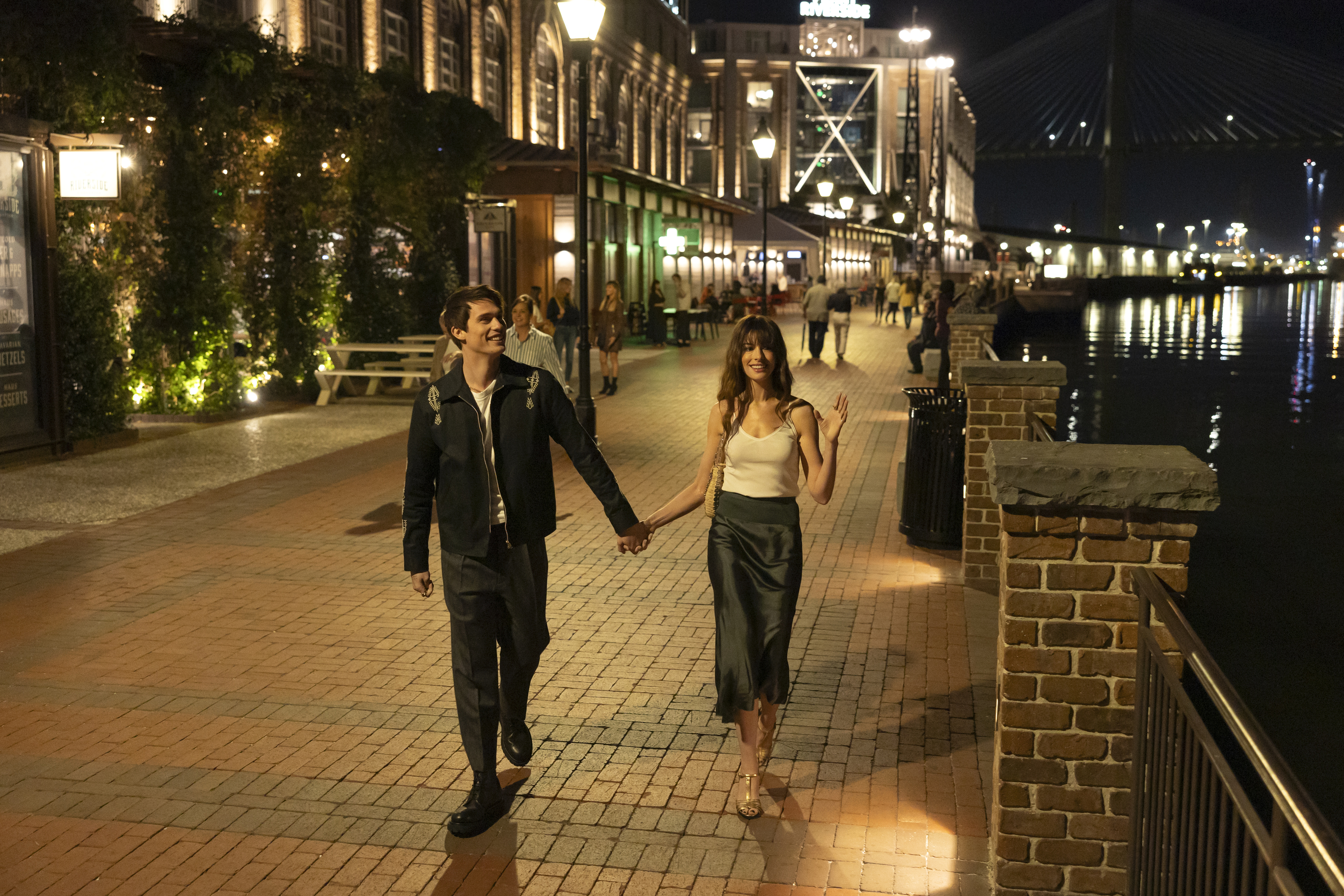 Nicholas Galitzine e Anne Hathaway em cena de Uma Ideia de Você; eles estão andando de mãos dadas pela rua durante a noite